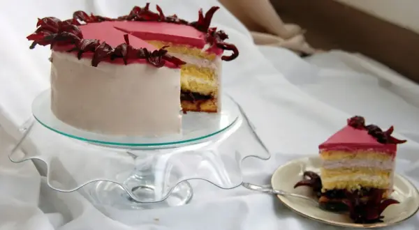 Różowy tort z kremem hibiskusowym, ozdobiony suszonymi kwiatami hibiskusa.