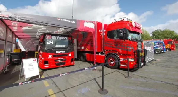 Deux camions de course rouges, prêts pour la vitesse max, sont garés sous une tente. L'un porte le numéro 24.
