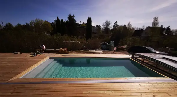 Arbetare bygger in pool med trädäck. Vattnet glittrar i solen. Snart redo för bad!