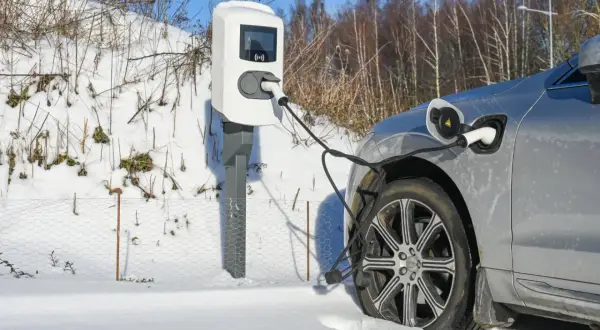 Une voiture électrique grise est branchée à une borne de recharge dans un paysage enneigé. Le chauffage de la voiture électrique est assuré par cette connexion.