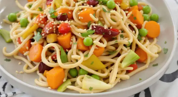 Assiette de nouilles sautées colorées avec carottes, petits pois, poivrons et garniture de sésame. Une recette facile et savoureuse.