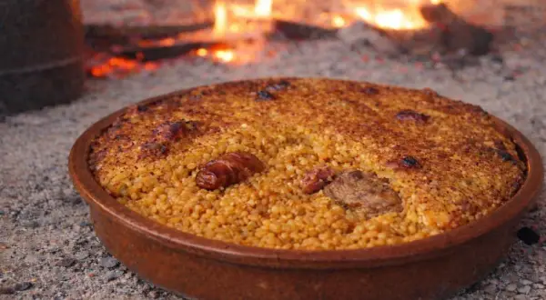 Arroz con costra recién hecho, con trozos de carne y salchicha, cocinándose a la leña.