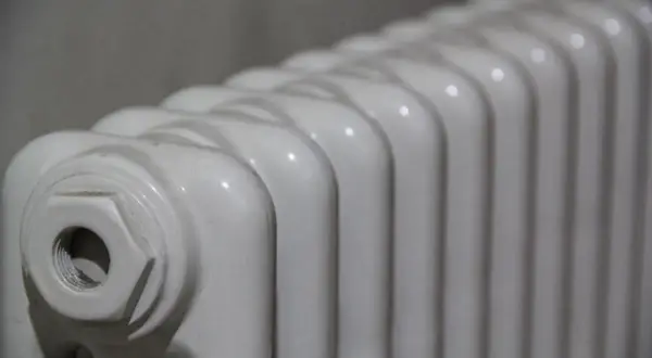 Radiador de mica blanco, con sus aletas curvas y un detalle de conexión en un extremo.