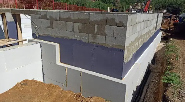 Izolacja fundamentów w starym domu w trakcie prac. Ściany z bloczków betonowych, styropian i hydroizolacja.