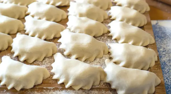 Rządki surowego ciasta na pierogi ułożone na desce, posypanej mąką.