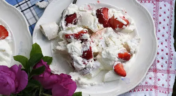 En härlig Eton Mess med färska jordgubbar och marängbitar, serverad på en vit tallrik med en vacker duk och rosor.