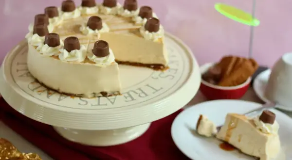 Eine köstliche Maxi King Torte, verziert mit Sahnetuffs und Schokostückchen, steht auf einem Tortenständer. Ein Stück ist bereits auf einem Teller angerichtet.
