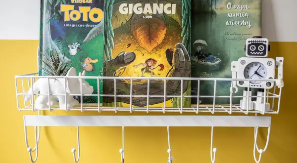 Na półce stoją komiksy do nauki czytania: "Toto i magiczne drzewo", "Giganci" i "O czym szumią wierzby". Obok robot-zegarek.