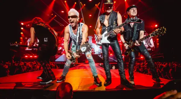 Zespół Scorpions na koncercie, grający swoje rockowe ballady. Wokalista z blond włosami i w okularach krzyczy do mikrofonu.