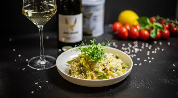 Kremowe risotto z kurczakiem i szparagami, udekorowane kiełkami. Obok kieliszek białego wina i butelka.