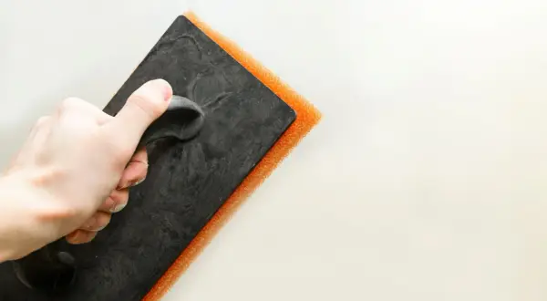 Mano che impugna una spatola con spugna arancione per la pittura tamponato.