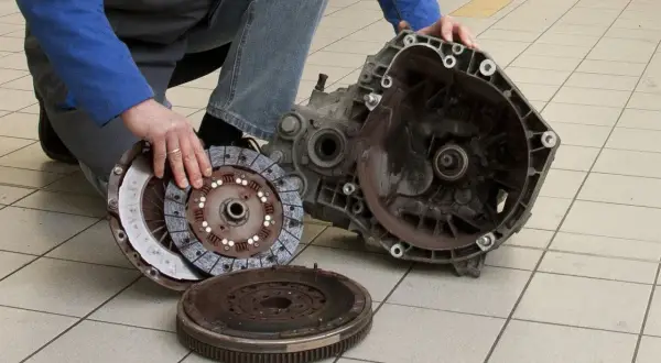 Mechanik pokazuje rozłożony zestaw sprzęgła i skrzynię biegów. Uszkodzony wysprzęglik objawy mogą być różne, ale ten element jest kluczowy.