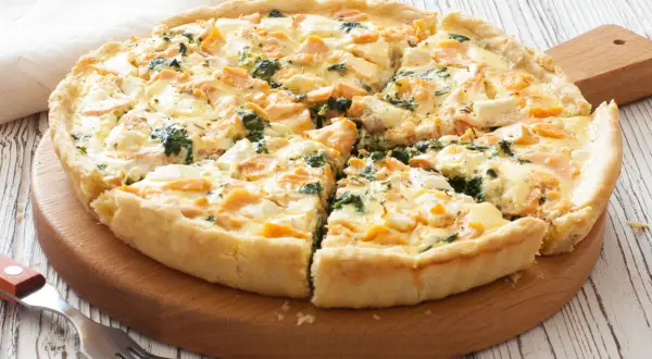 Pyszna tarta z łososiem, szpinakiem i serem feta, pokrojona na kawałki, na drewnianej desce.