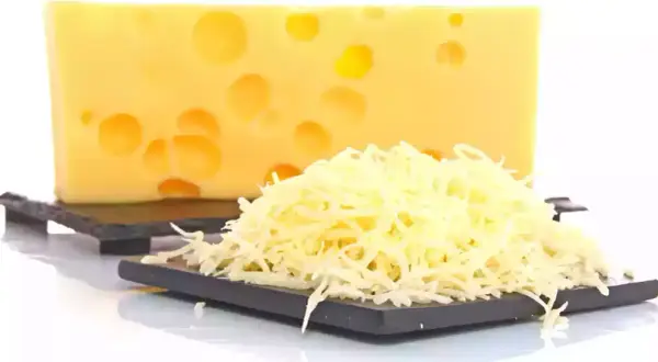 Bloque de queso suizo con agujeros y una pila de queso rallado, listo para ser queso que se derrite.