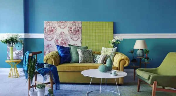 Soggiorno con divano giallo, cuscini verdi e blu, e pareti blu. Ottime idee per colorare le pareti di casa con contrasti vivaci.