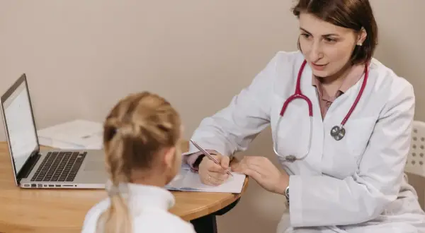 Lekarka pisze zwolnienie lekarskie do szkoły dla małej pacjentki.