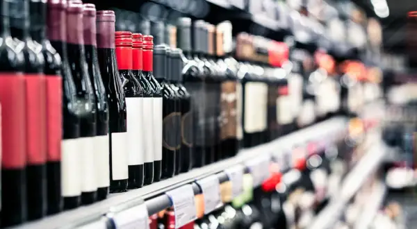 Rzędy butelek wina na półce sklepowej. Widać etykiety i ceny alkoholu, zachęcające do wyboru.