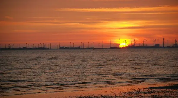 Sonnenuntergang am Emden Strand mit Windrädern und glitzerndem Wasser.