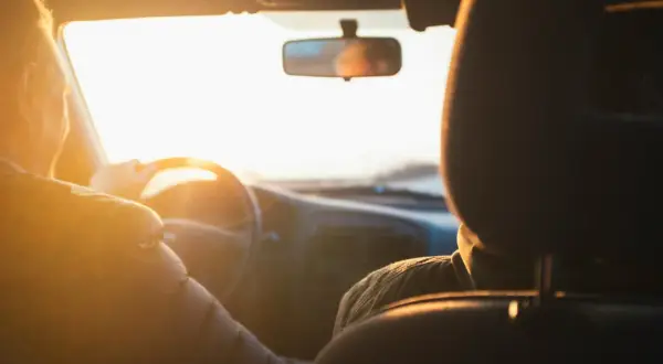 Två personer i en bil i solnedgången. Föraren håller i ratten. Vad betyder begagnad? Kanske bilen är begagnad, men resan är ny.