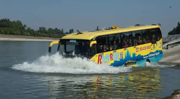 Żółty autobus "River Ride" wjeżdża do wody, tworząc fontannę. To niezwykła atrakcja turystyczna, która zabiera pasażerów na wycieczkę po Dunaju w Budapeszcie.