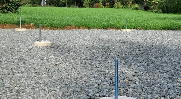 Gotowe fundamenty z betonu pod słupy wiaty, osadzone w żwirze.