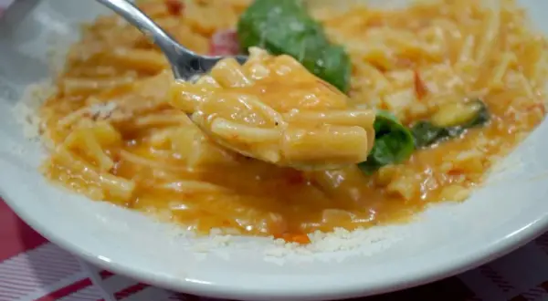 Un cucchiaio di pasta con patate cremosa, condita con basilico fresco e parmigiano grattugiato.