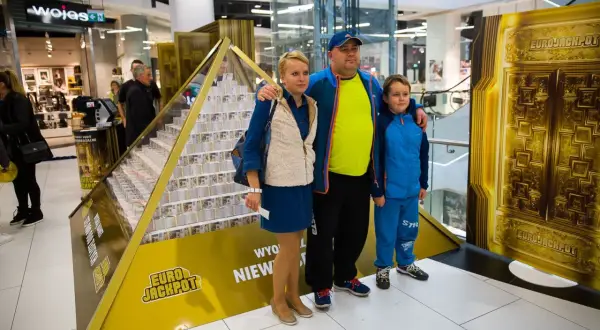 Rodzina pozuje przy piramidzie z pieniędzy, symbolizującej wygraną w Eurojackpot. Dowiedz się, eurojackpot jak odebrać wygraną.