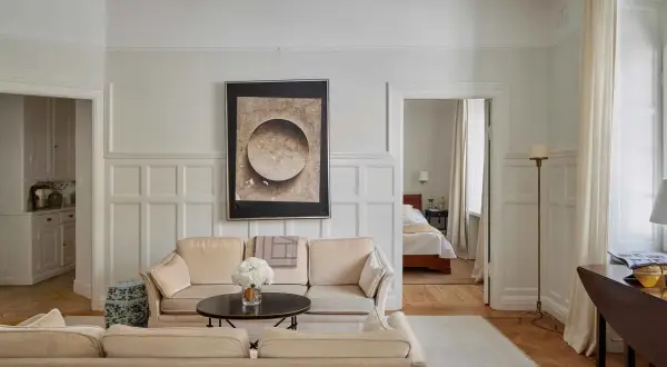Vardagsrum med beigefärgad soffa, konstverk och en öppen dörr till sovrum. En vacker renovering av ett sekelskifteshus.