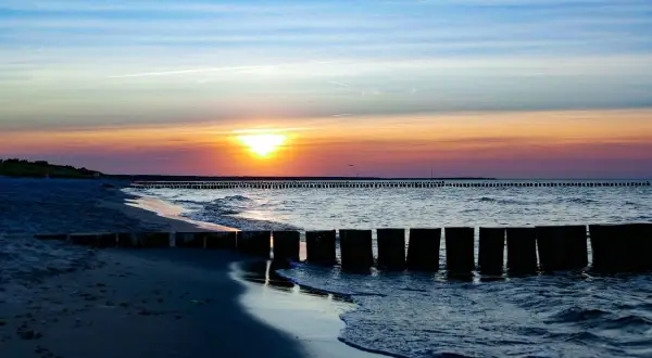 Zachód słońca nad Bałtykiem w Sarbinowie. Drewniane falochrony i pusta plaża tworzą malowniczy krajobraz, idealny na wieczorny spacer. To jedne z wielu sarbinowo atrakcje.