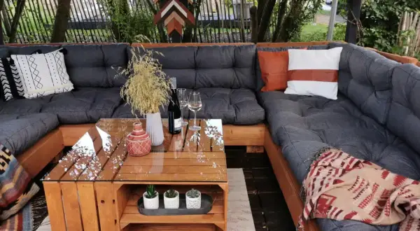 Gemütliches Palettensofa bauen: Eine Lounge-Ecke im Garten mit Glas-Couchtisch, Kissen und Decken. Perfekt für entspannte Stunden.