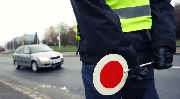Agent de police en uniforme, gilet fluorescent, tenant un panneau stop. Contrôle routier, papier obligatoire.