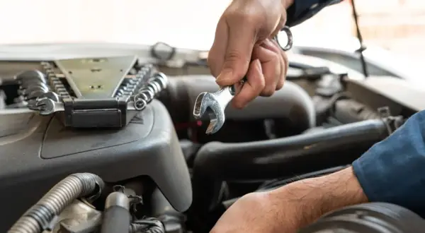 Mechanik dokonuje wymiany sprężarki klimatyzacji, używając klucza do odkręcenia śrub w silniku samochodu.