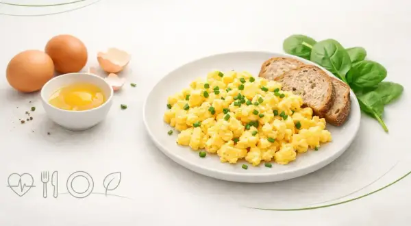 Jajecznica na talerzu z pieczywem i szpinakiem, obok surowe jajka.