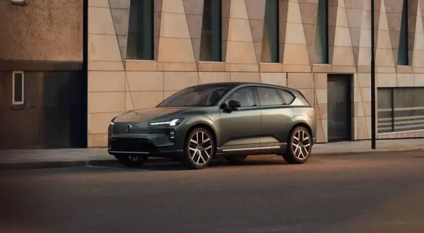 Elegante Volvo EX60 verde metallizzato parcheggiata davanti a un edificio moderno con facciata geometrica.