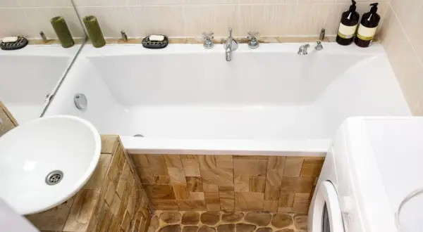 Badezimmer mit Waschbecken, Badewanne verkleiden mit Naturstein und Waschmaschine.