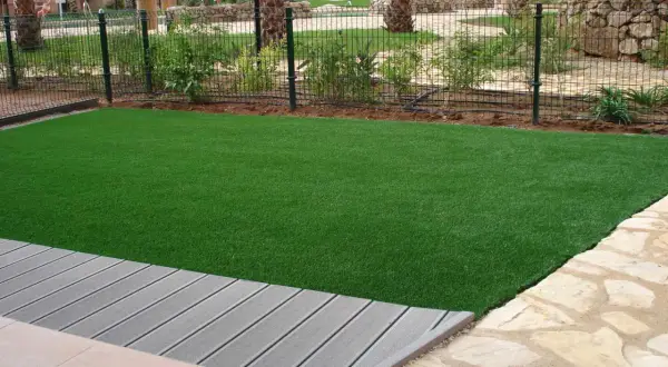 Césped artificial verde vibrante junto a una terraza de madera gris. El césped artificial puede generar electricidad estática.