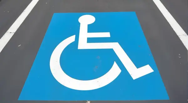 Symbole de fauteuil roulant blanc sur fond bleu, marquant une place de stationnement réservée. Une amende place handicapé est une infraction.