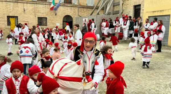 Un uomo con un costume da toro guida una sfilata di bambini vestiti di rosso e bianco per il carnevale nelle Marche.
