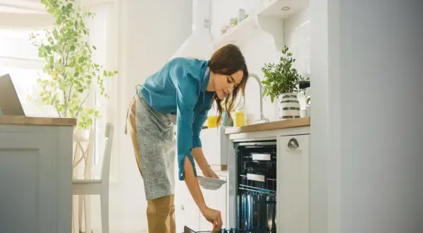 Kobieta wkłada talerz do zmywarki. Zastanawia się, czy lepsza będzie zmywarka 45 czy 60 cm.