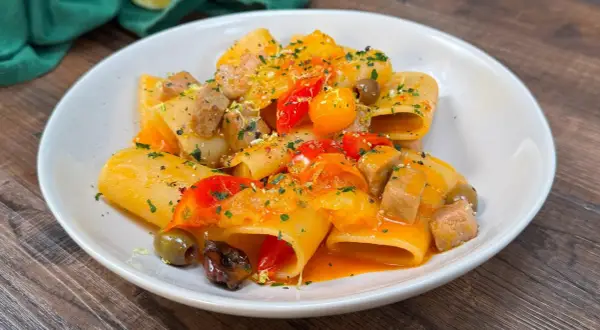 Paccheri con tonno fresco, pomodorini, olive e scorza di limone. Un piatto colorato e saporito, pronto per essere gustato.