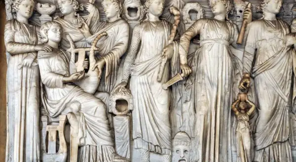 Kamienna płaskorzeźba przedstawia grupę kobiet, w tym Demeter i Korę, otoczone instrumentami muzycznymi i symbolicznymi przedmiotami.