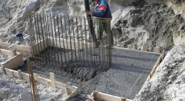 Budowa fundamentów: pracownik wylewa beton do szalunku zbrojonego.