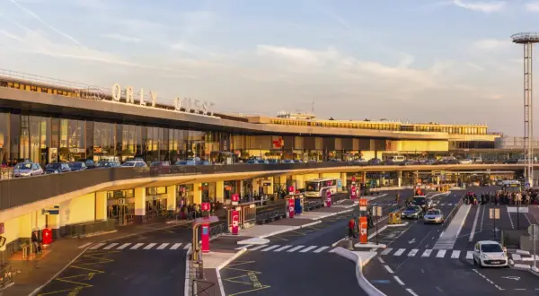 Orly Ouest, jedno z lotnisk w Paryżu, tętni życiem. Samochody i autokary czekają na pasażerów przy nowoczesnym terminalu.