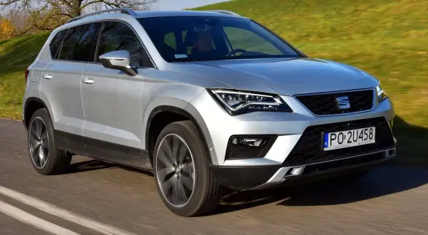 Srebrny Seat Ateca w ruchu. Kierowca za kierownicą, zielone wzgórza w tle. Wiele osób szuka seat ateca opinie przed zakupem.