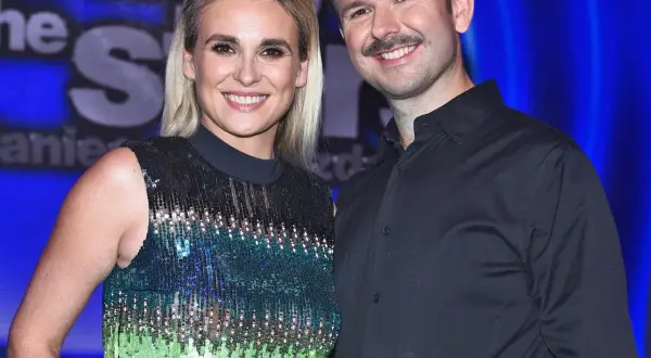 Sławomir i Kajra uśmiechają się do aparatu na tle niebieskiego tła.