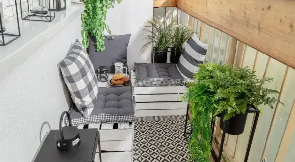 Przytulny balkon w bloku z wygodnymi siedziskami z palet, mnóstwem zieleni i czarno-białymi dodatkami. Idealne miejsce na poranną kawę.