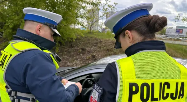 Policjanci w kamizelkach odblaskowych sprawdzają dokumenty, być może wystawiają mandaty za prędkość.