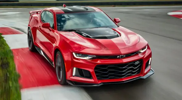 Czerwone Camaro ZL1 z czarnymi pasami na masce i dachu, pędzące po torze wyścigowym.