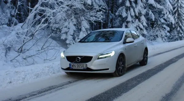 Białe Volvo V40 D3 pokonuje ośnieżoną drogę w lesie.