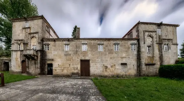 Las Torres de Allo, un edificio de piedra con un balcón ornamentado y ventanas blancas, se alza bajo un cielo nublado y dinámico.